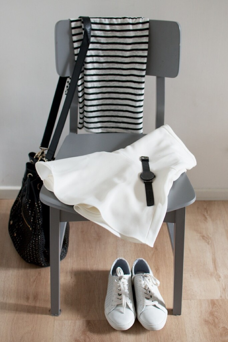 One outfit staged on a grey chair: striped top, white skirt, black bag, watch and white sneakers