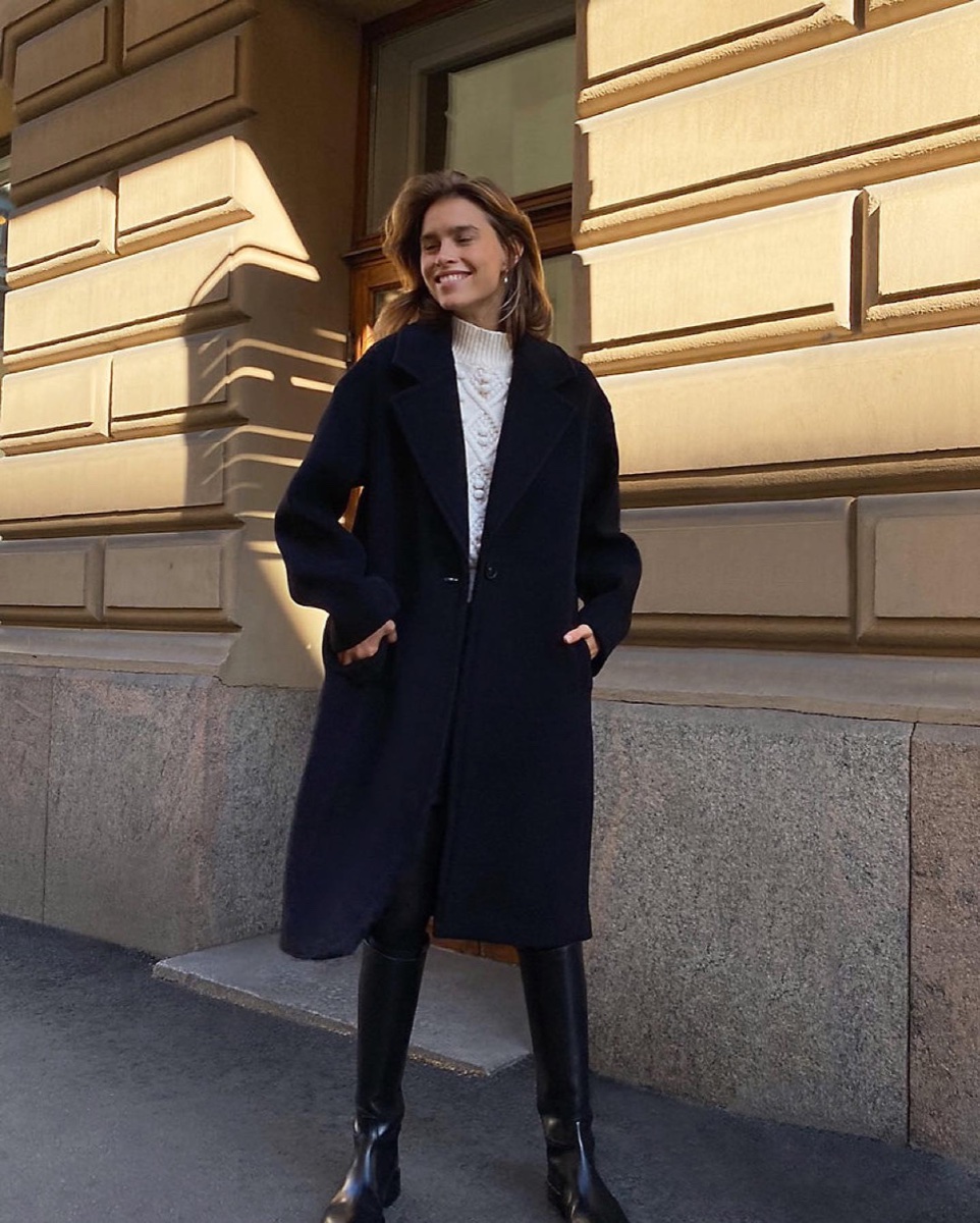 A navy Italian-wool coat over a cream cable knit, autumn sun on a stone facade