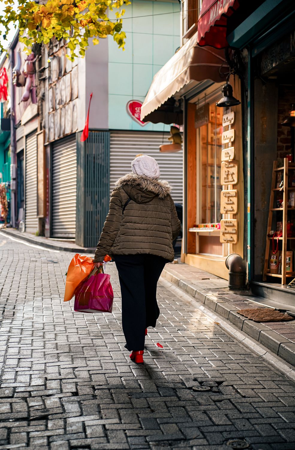 A shopper walking away down an autumn street carrying two paper shopping bags