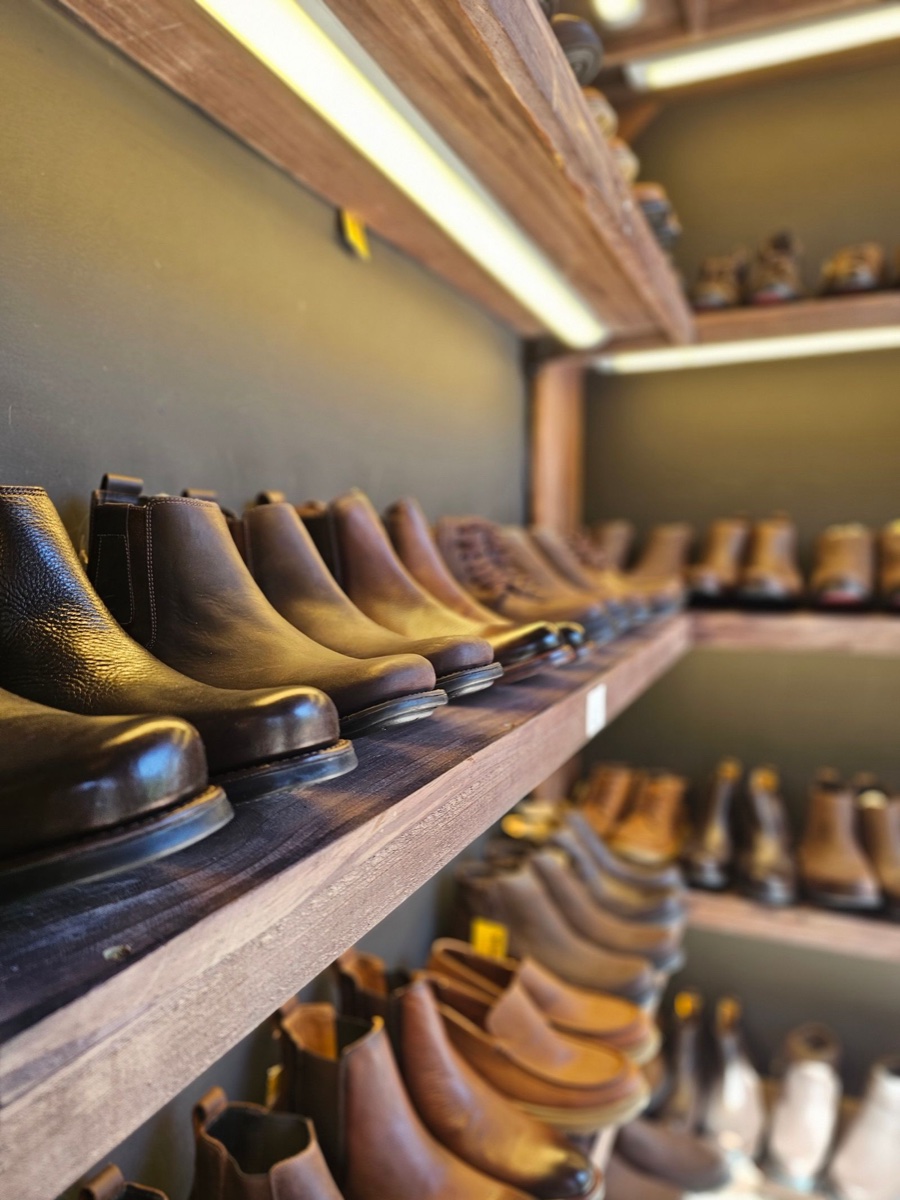 Rows of brown and black leather chelsea boots lined up on wooden shelves in a warmly lit shoe shop