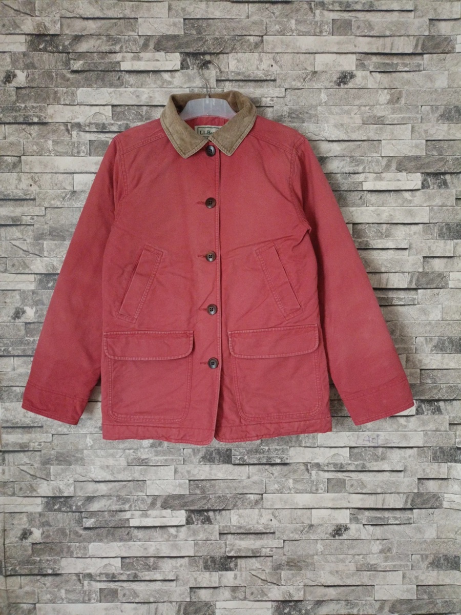 A faded red vintage L.L.Bean barn jacket with a tan corduroy collar hanging on a stone-tile wall