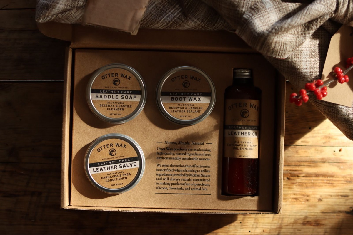 A boxed set of wax and leather care tins and oil in warm window light on a wooden table
