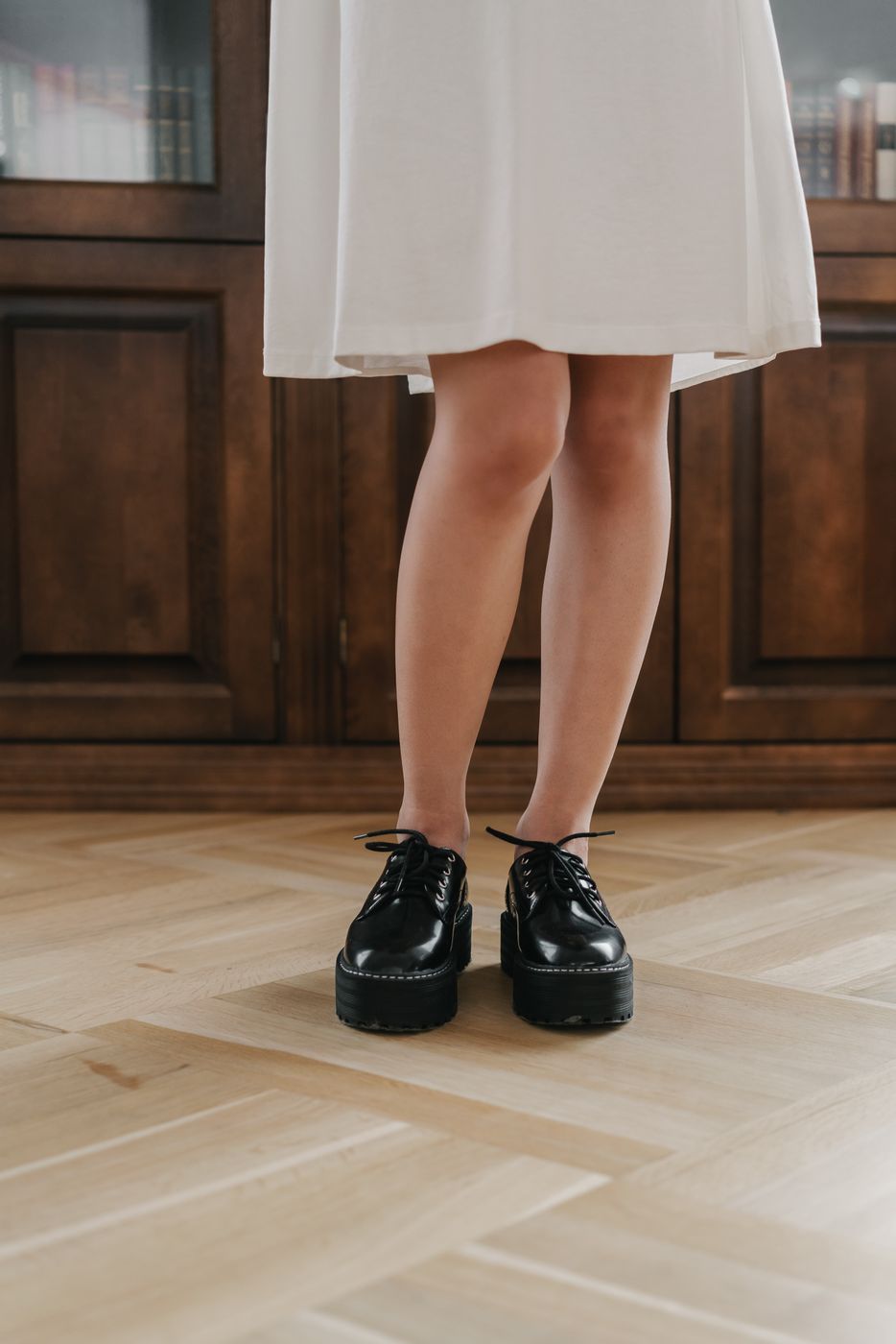 Woman in a white dress standing on herringbone parquet in black lace-up derby shoes