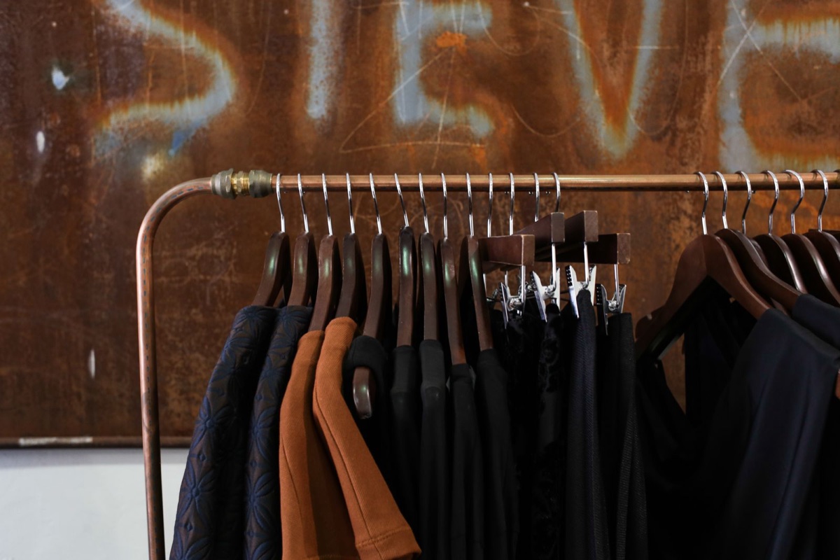 A clothes rack of mostly black garments on wooden hangers with a single rust-brown piece near the end