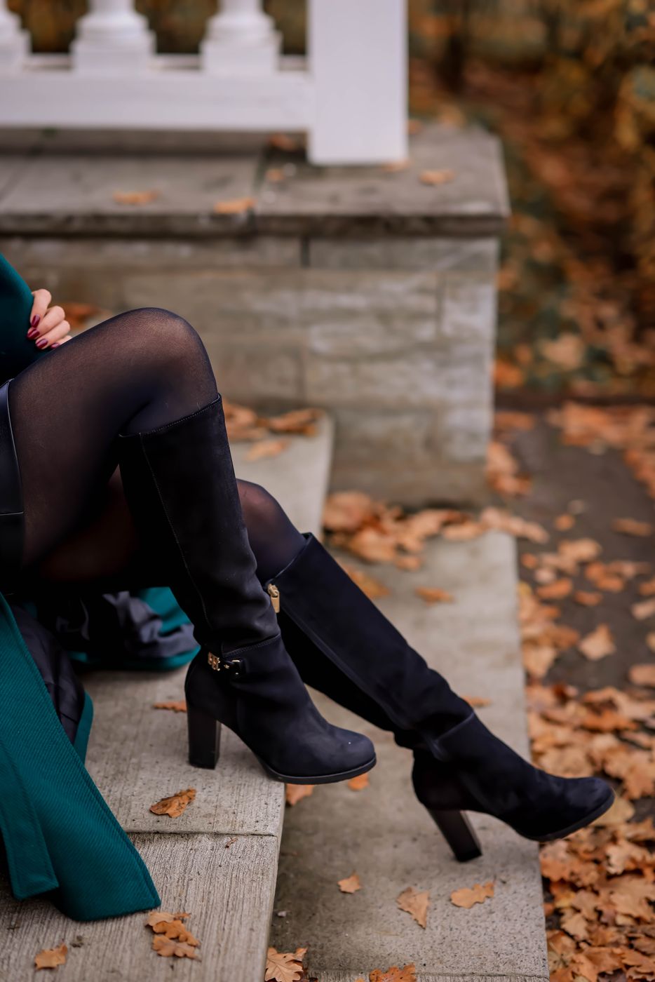 Legs in dark sheer tights and black suede knee boots on stone steps covered in fallen leaves