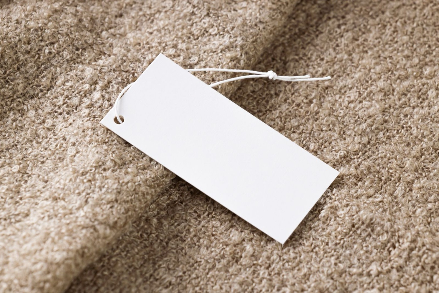 A blank white price tag on a string lying on beige bouclé fabric