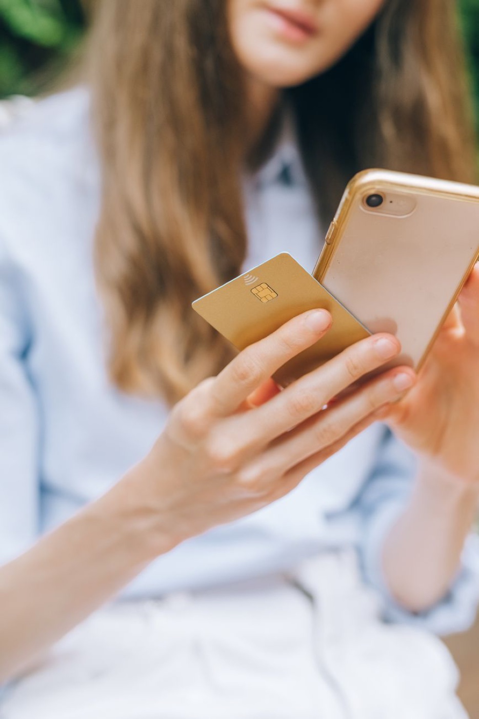 A person's hands holding a gold payment card against the back of a smartphone