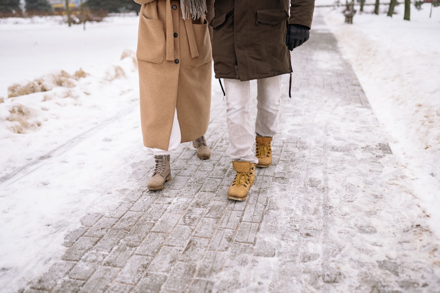 Two people walking away on a snow-dusted brick path, one in tan lace-up boots and one in yellow work boots