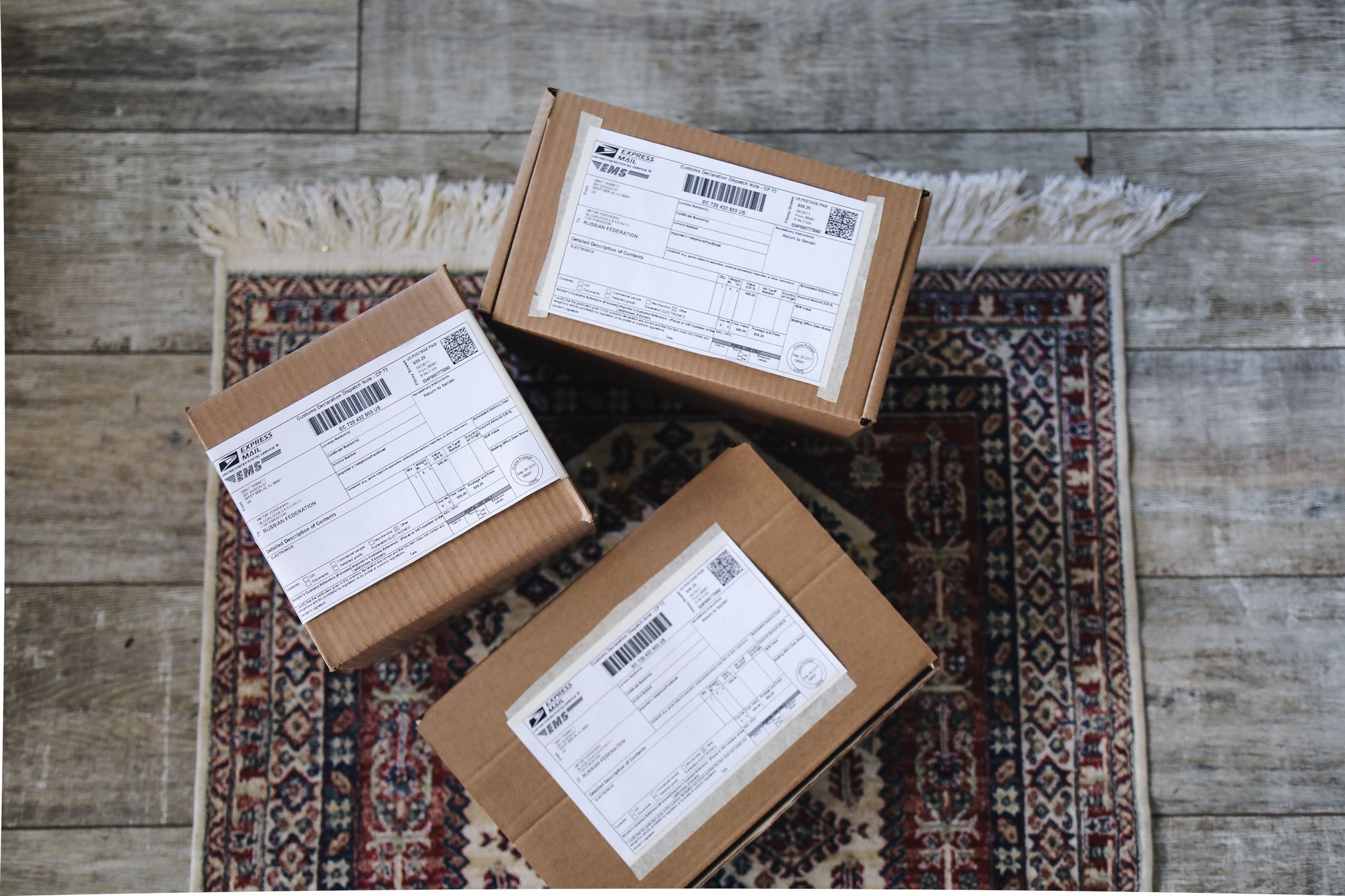 Three cardboard boxes with USPS Express Mail labels arranged on a patterned rug