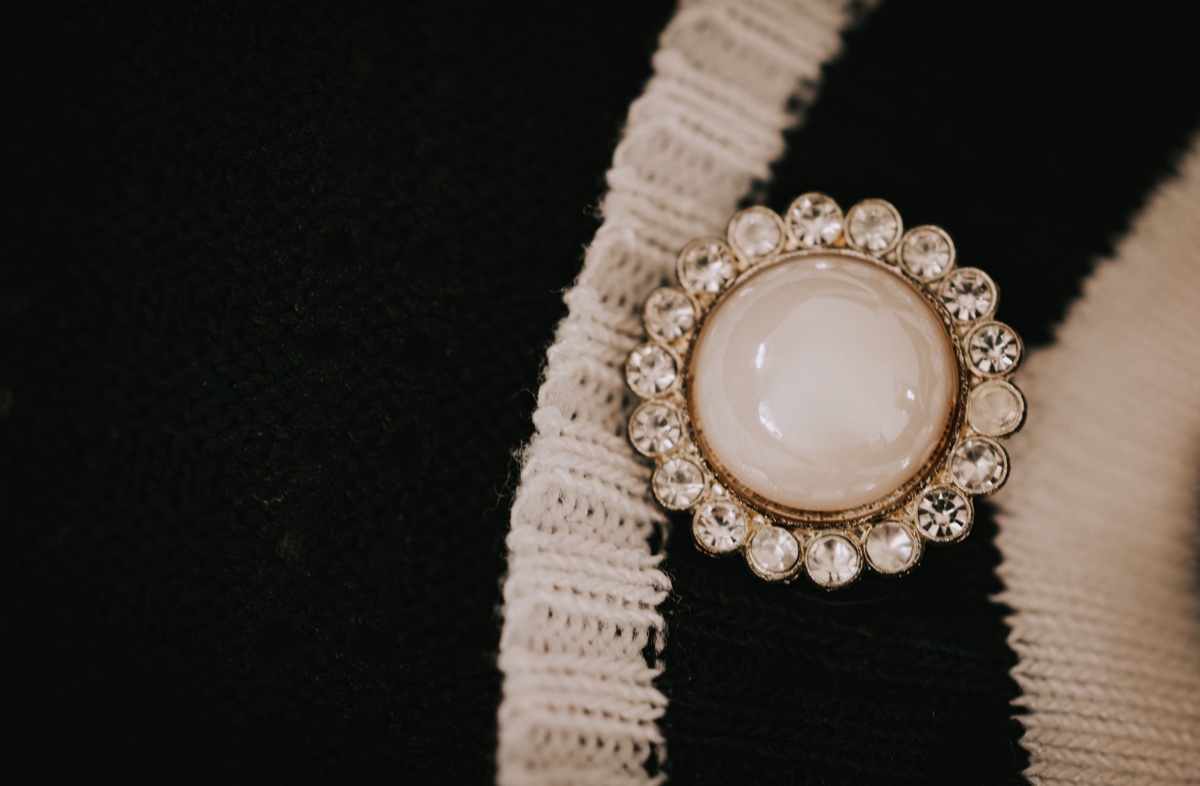A round pearl brooch ringed with small rhinestones pinned to a black knit with white lace trim, photographed close up
