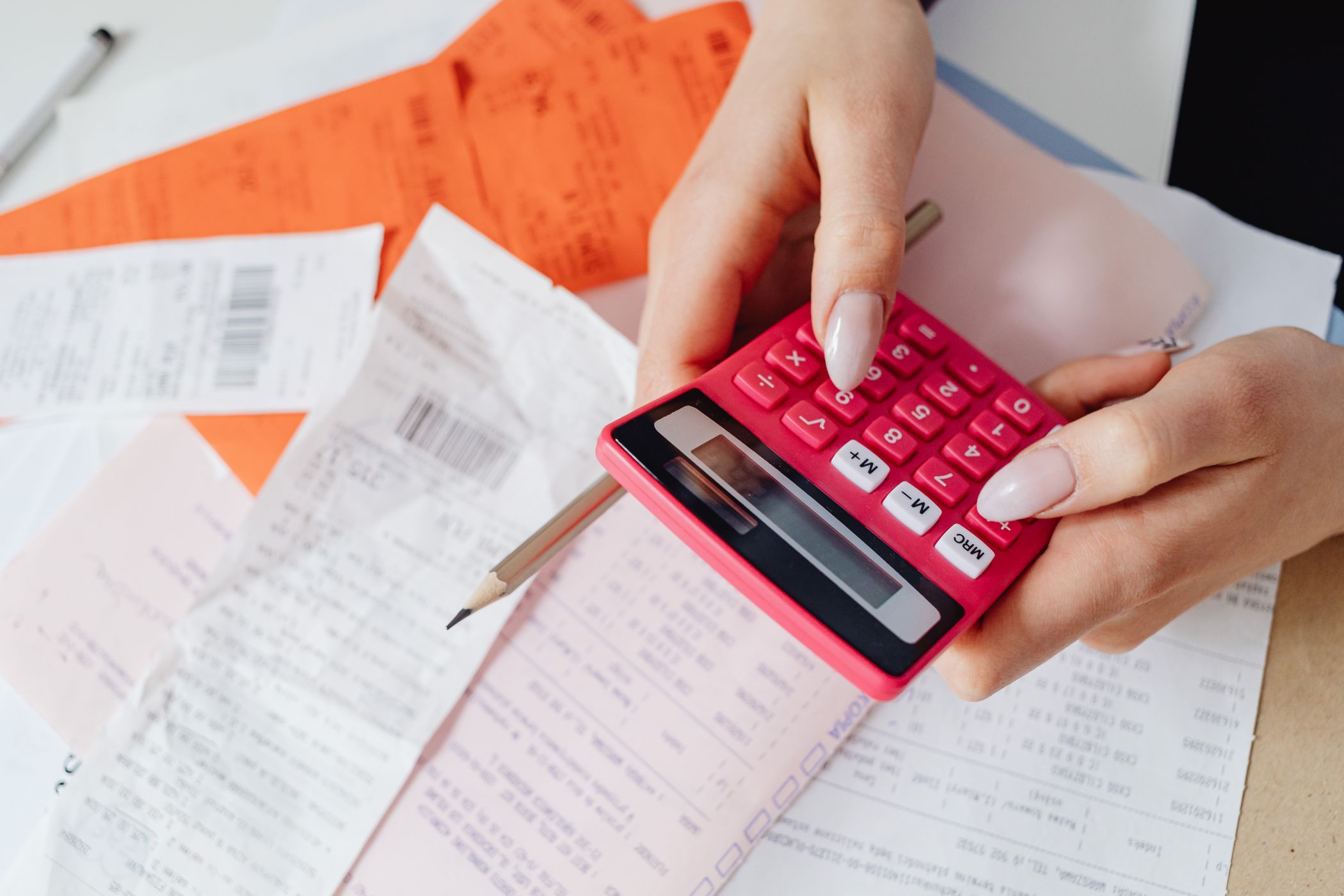 Hands working a small pink calculator over a desk scattered with store receipts