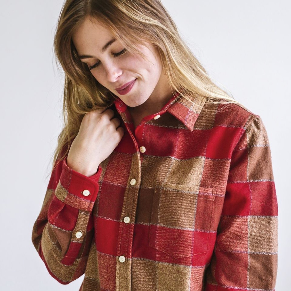 A model in a red and camel plaid flannel shirt, buttoning the collar