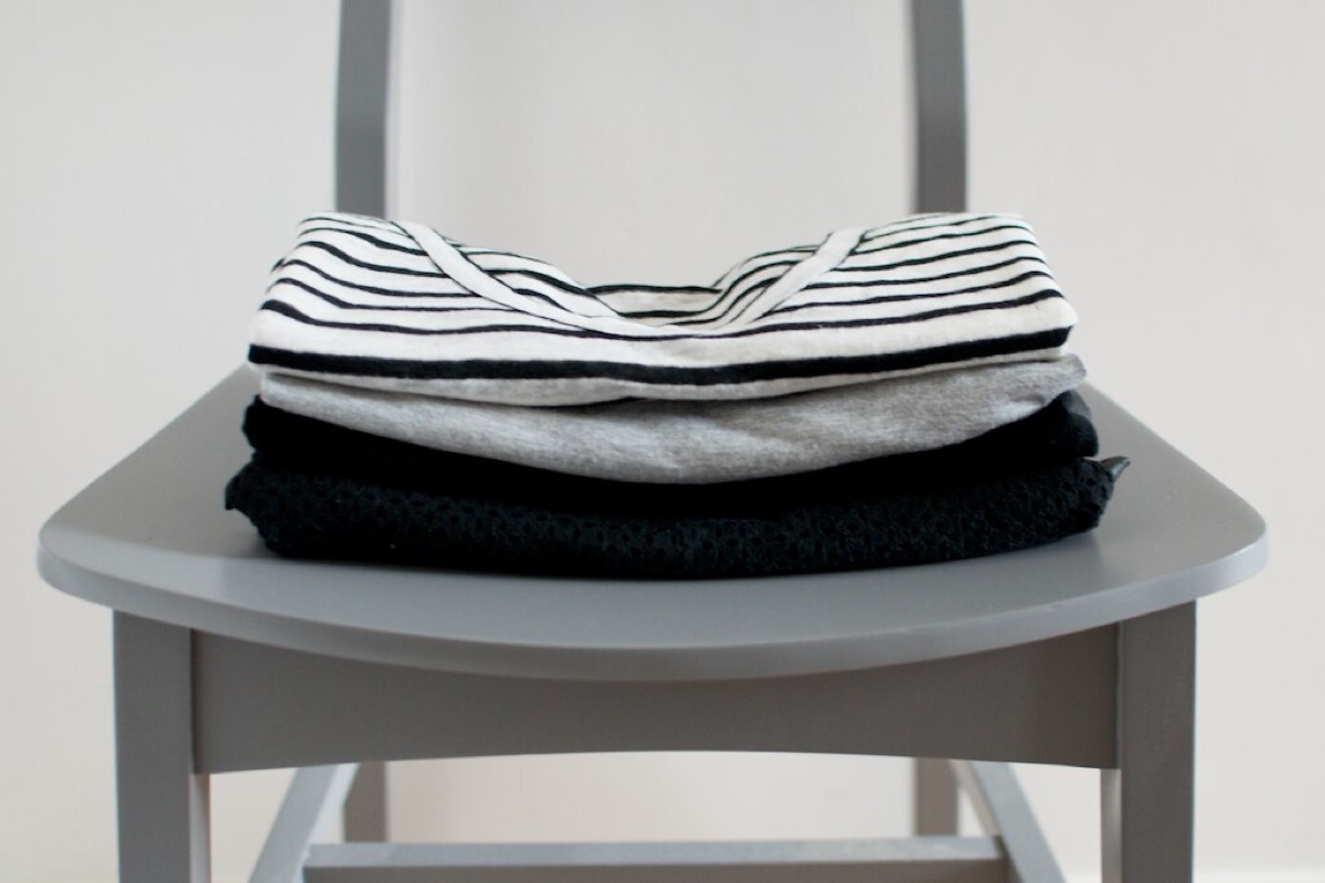 Three folded tops, striped, grey and black, stacked on a grey chair
