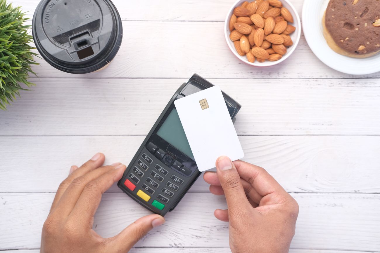 Hands holding a blank white chip card over a payment terminal on a white wooden table