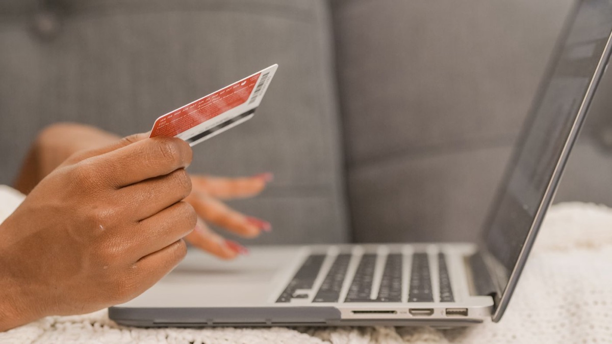 A hand holds a red loyalty card beside a laptop keyboard in warm indoor light