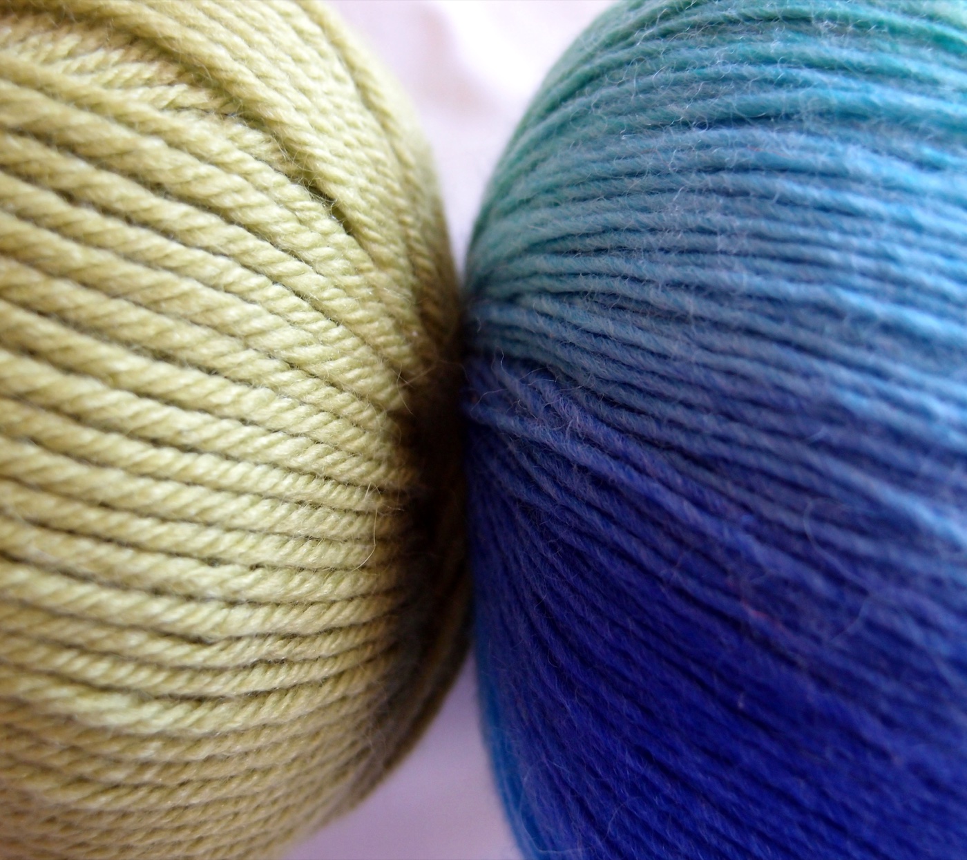 Two balls of wool side by side, the left one showing four strands visibly twisted around each other, the right one a single fuzzy untwisted strand