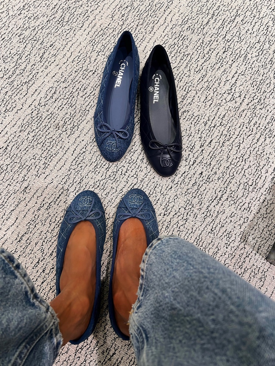 Three pairs of Chanel ballet flats on a boutique carpet, one denim pair worn and a quilted denim and navy leather pair beside it