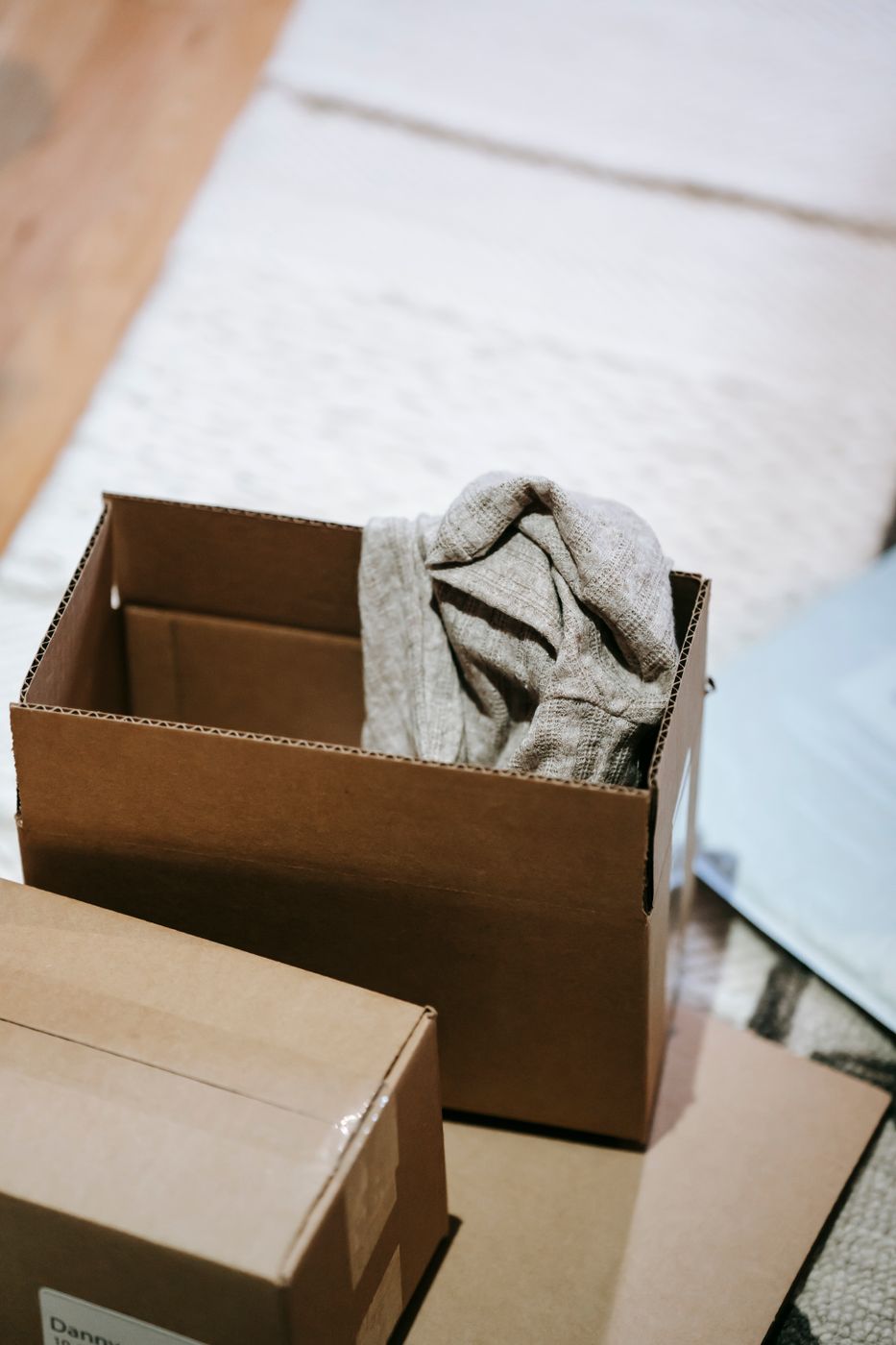 Open cardboard shipping box on a carpet with a gray knit garment inside