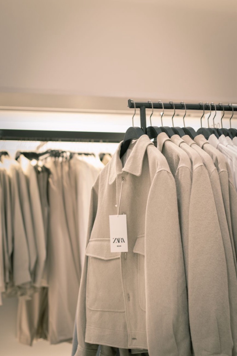 Oatmeal wool overshirts hanging in a row on a shop rail, the front one showing a white Zara swing tag
