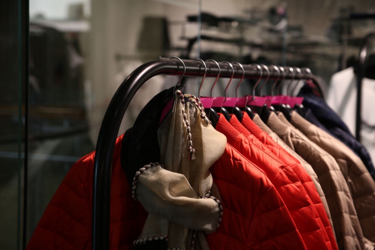 Padded jackets in red, camel and navy hanging on a metal rail in a shop, a cream scarf draped over the nearest hanger