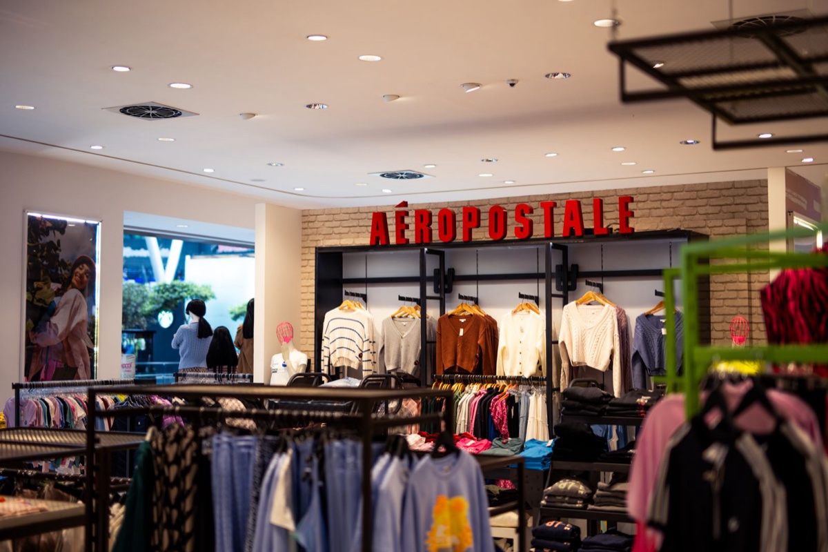 Clothing store interior with knit sweaters hung on wooden hangers along a brick back wall and folded jeans on tables below