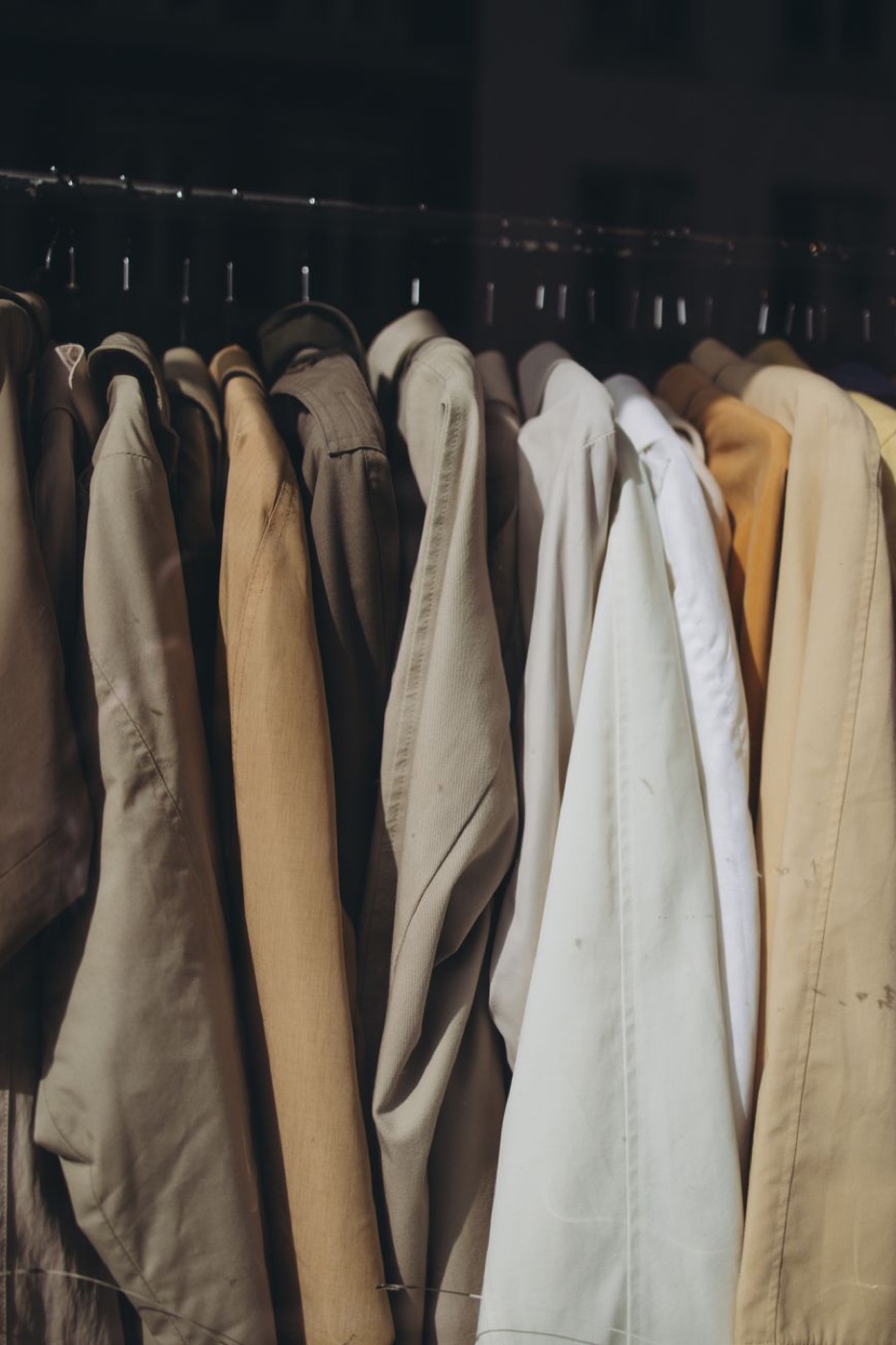 A row of beige, cream and tan coats and jackets hanging close together on a metal store rack in daylight