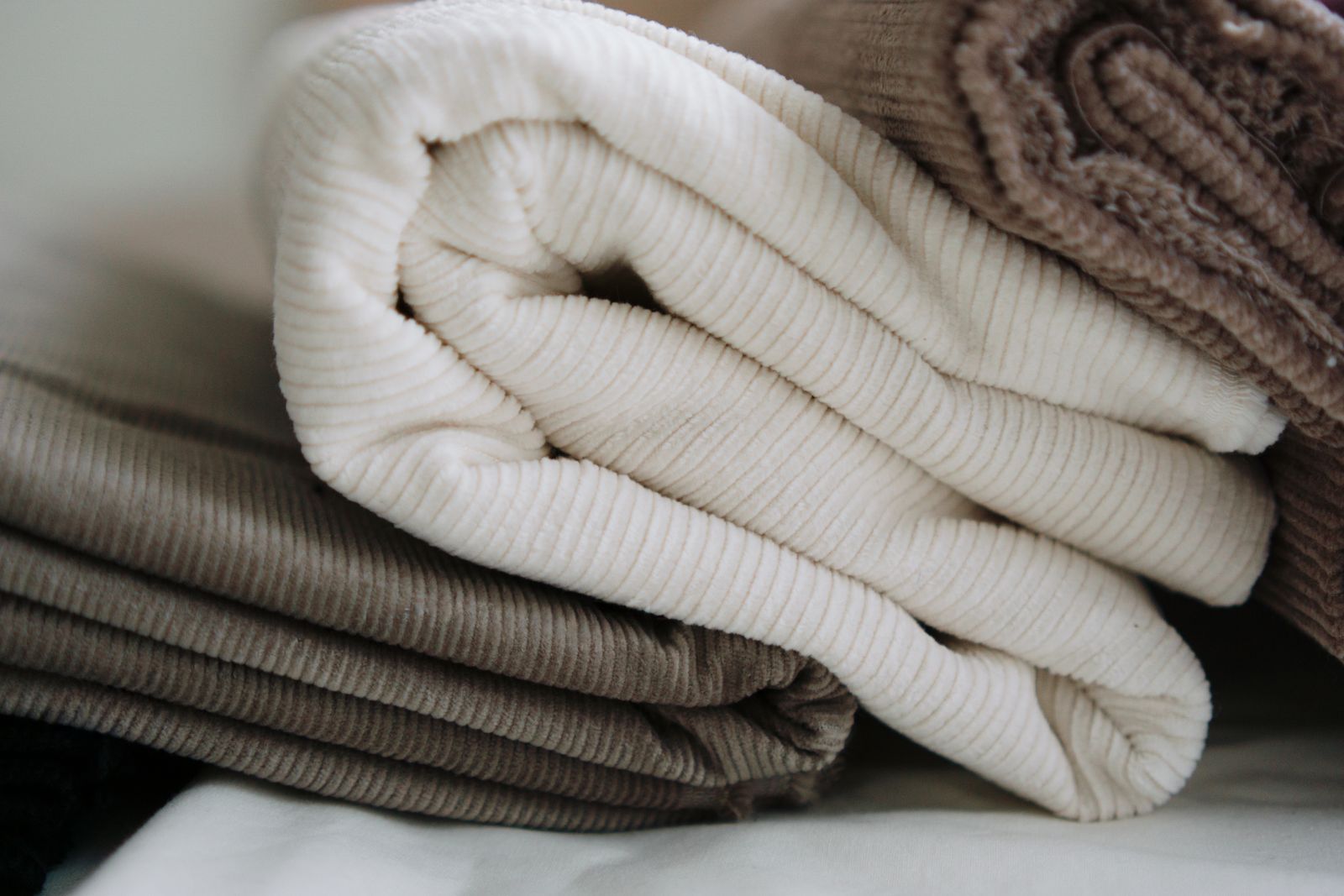 Folded rolls of corduroy fabric in cream, taupe and brown with the ribs running in parallel lines