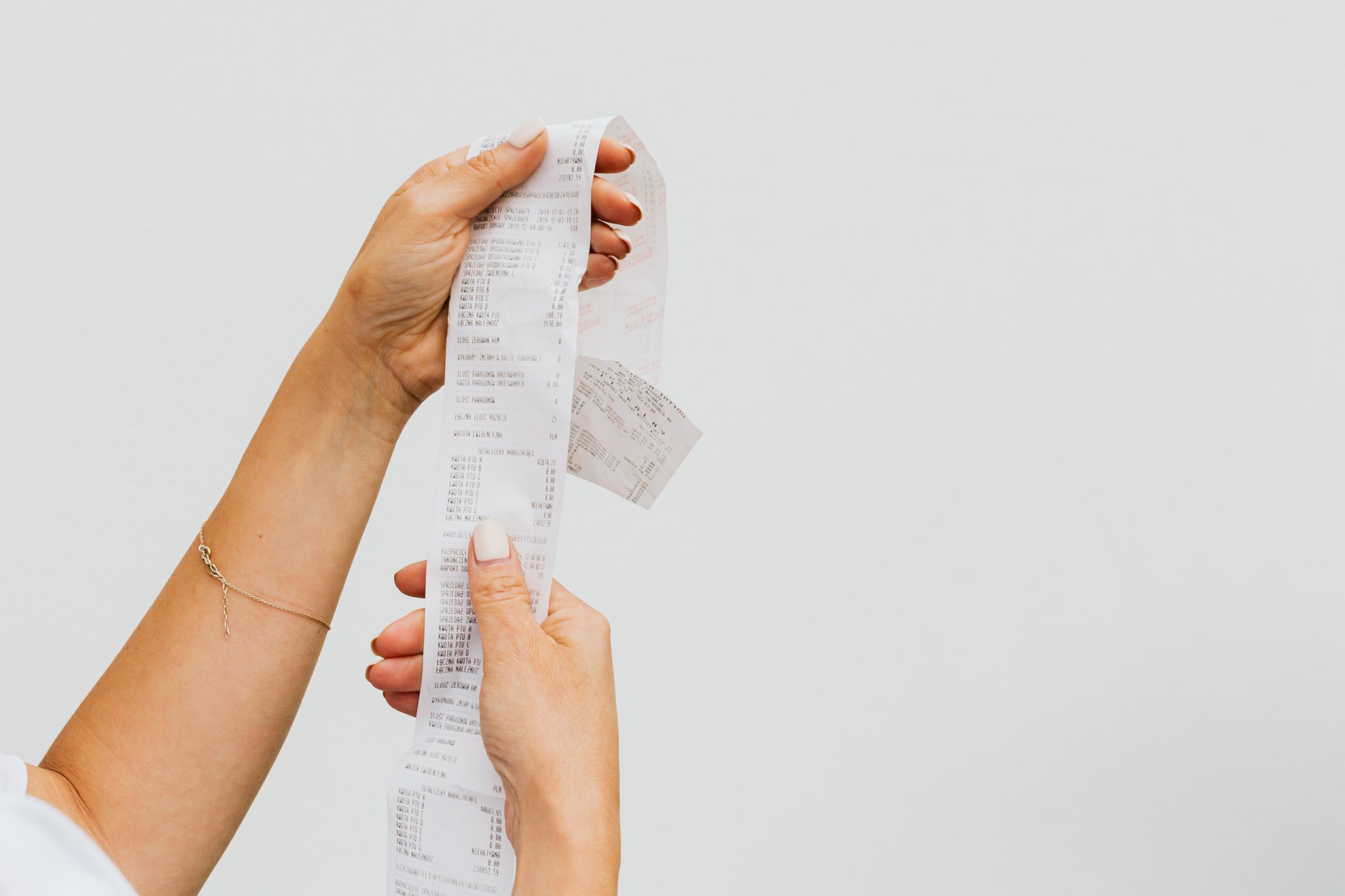 Two hands holding up a long unrolled paper till receipt against a plain pale background