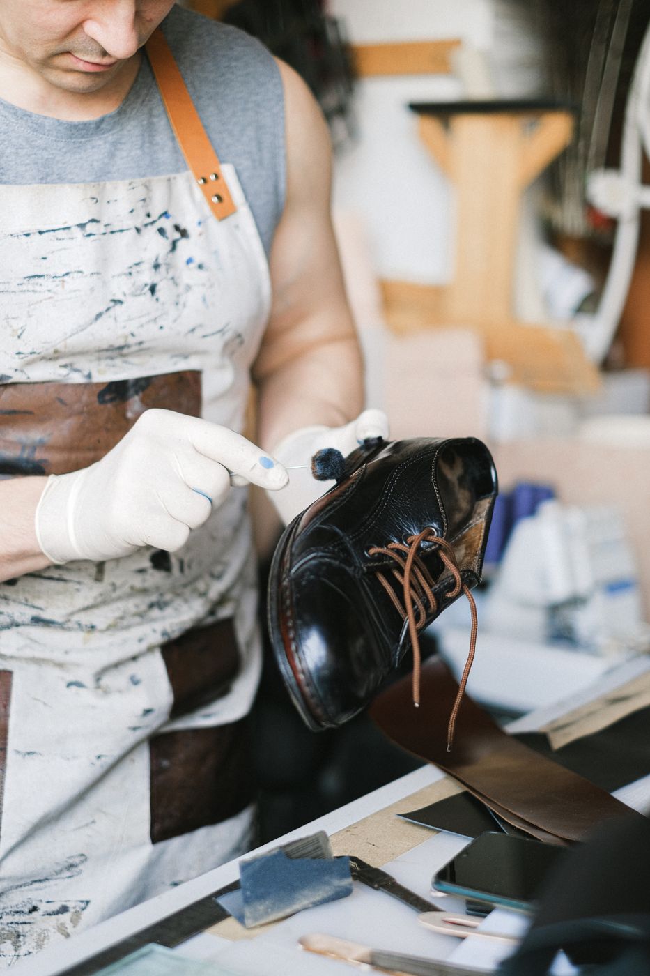 Craftsman in an apron and white gloves polishing a black leather lace-up shoe at a workbench