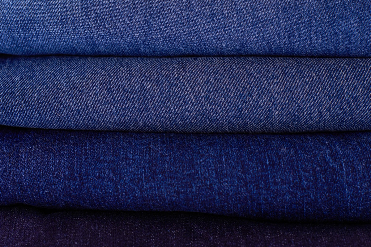 Close-up of four pairs of folded jeans stacked from mid-blue to nearly black dark wash