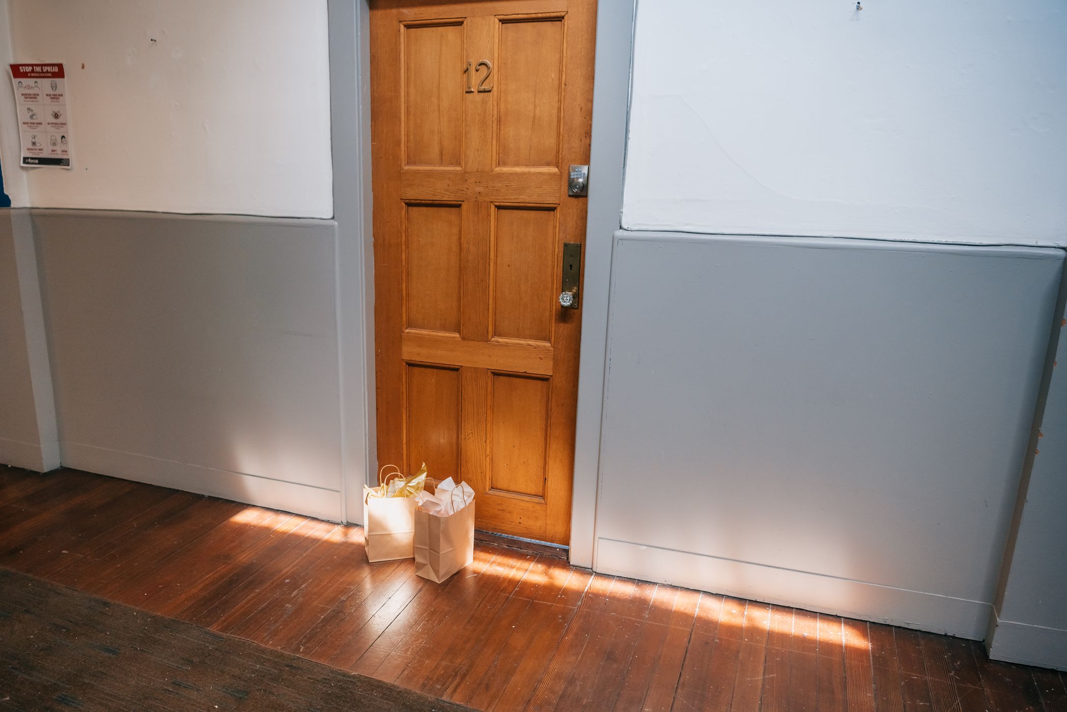 Paper shopping bags left on the doorstep of an apartment with a wooden door, lit by warm sunlight
