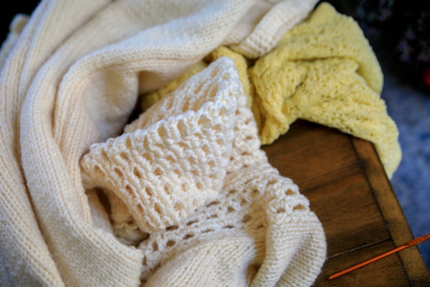 Cream and pale yellow knitted sweaters folded loosely on a dark wooden surface
