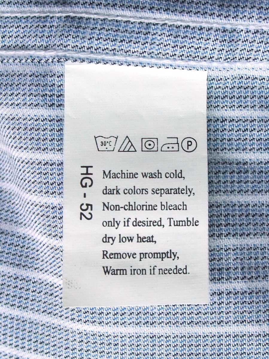 A white care label stitched into a blue and white shirt reading Machine wash cold, dark colors separately, non-chlorine bleach only if desired, tumble dry low heat, remove promptly, warm iron if needed