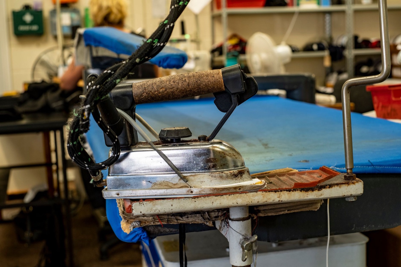 A heavy industrial steam iron resting on the edge of a blue padded pressing table in a garment workshop
