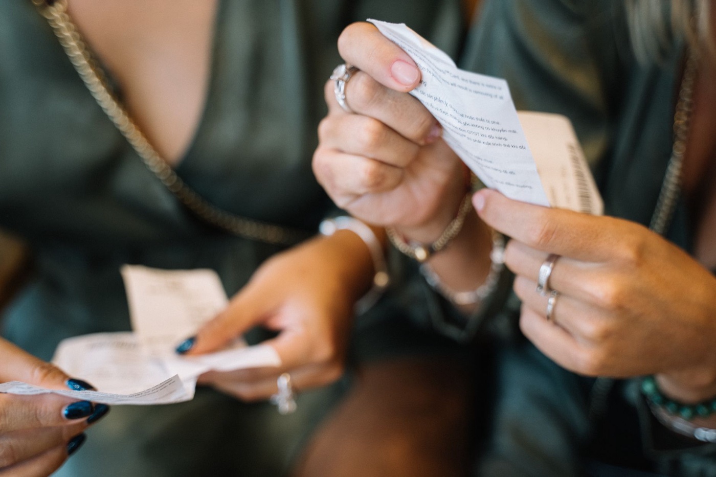 Close-up of two people's hands holding folded printed paper slips, faces out of frame, in warm indoor light