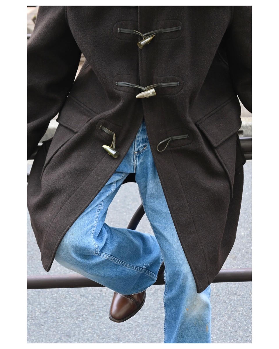 Close-up of horn toggles and leather loops on a dark brown wool duffle coat worn over faded blue jeans