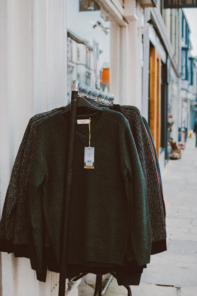 Dark green and marled knit jumpers on a rail outside a shop on a British street, a paper swing tag with a printed price hanging from the front one