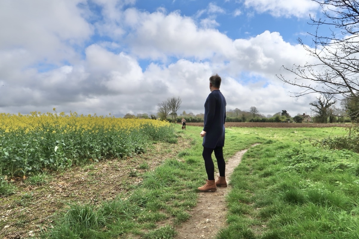A person seen from behind on a countryside path, wearing a navy sweater dress, dark tights and tan suede ankle boots