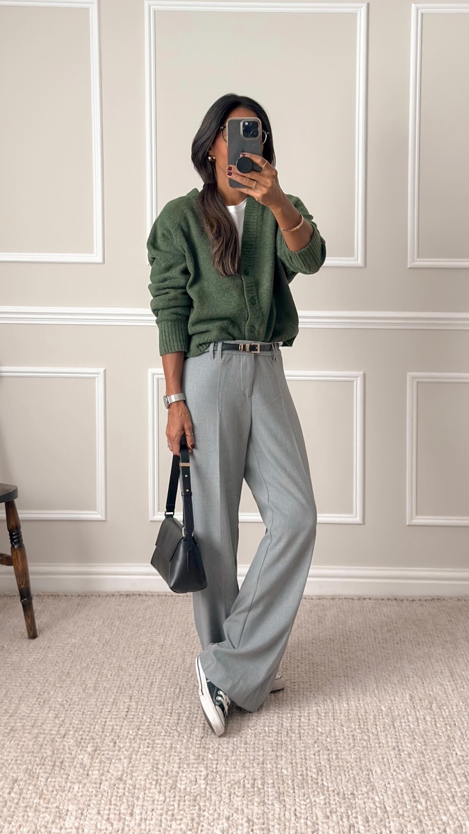 Mirror photo of a green zip cardigan worn with grey wide-leg trousers and black sneakers, in a pale panelled room
