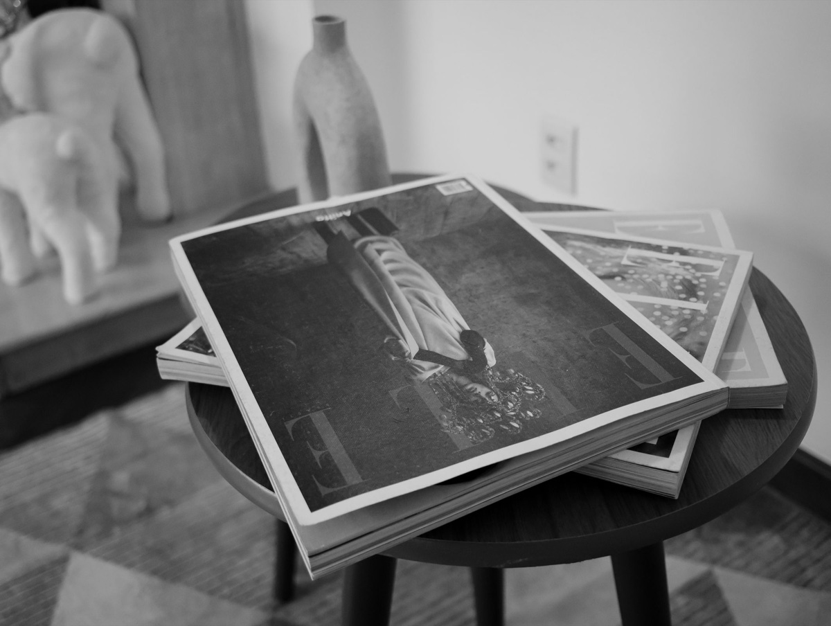 Black and white photo of fashion magazines stacked casually on a small round side table