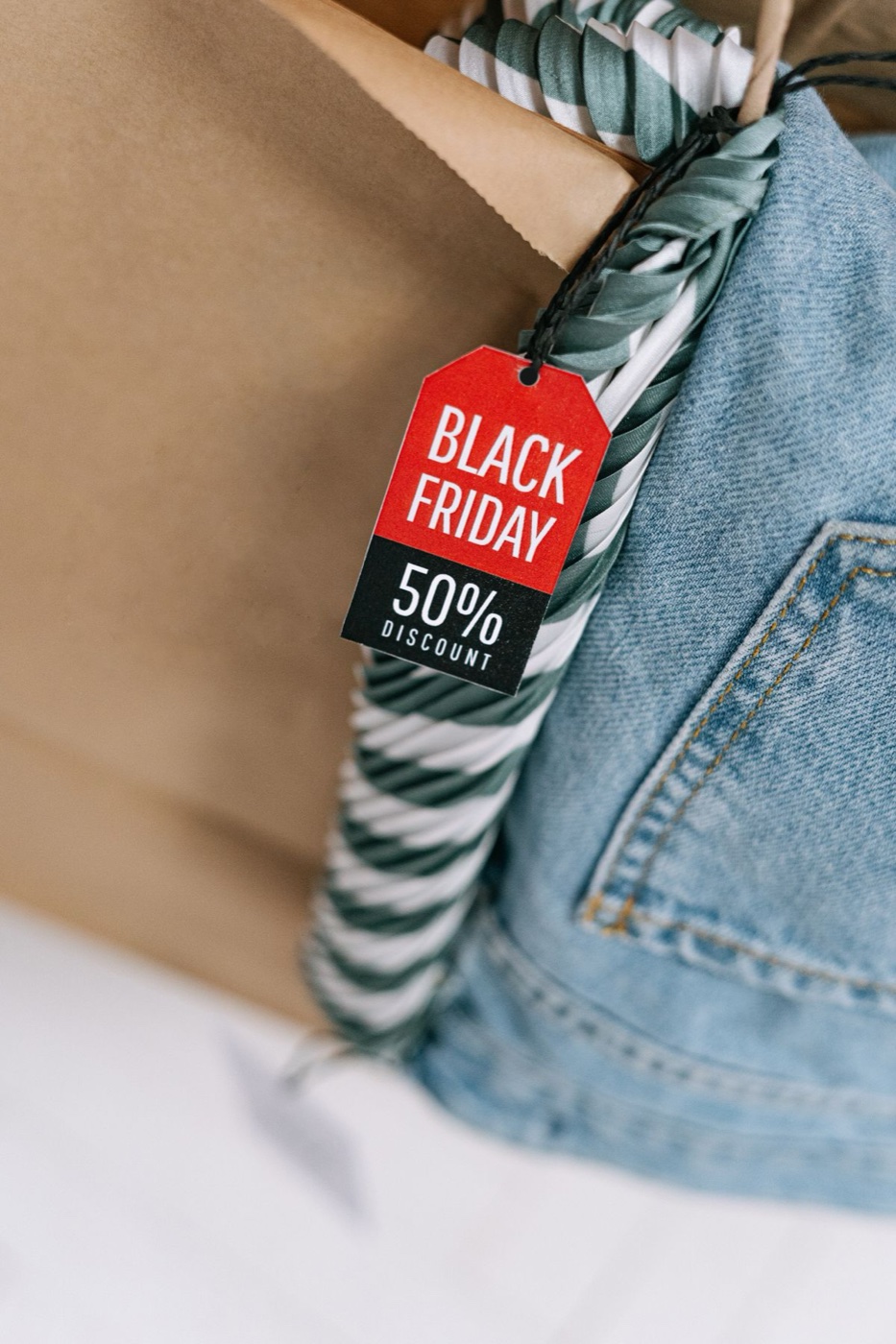 Close-up of a red and black printed 50 percent discount tag resting on light-wash denim inside a brown paper shopping bag