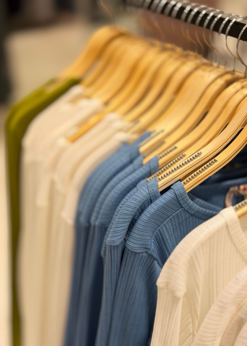 Close-up of ribbed knit tops in olive, white and blue on wooden hangers along a store rail