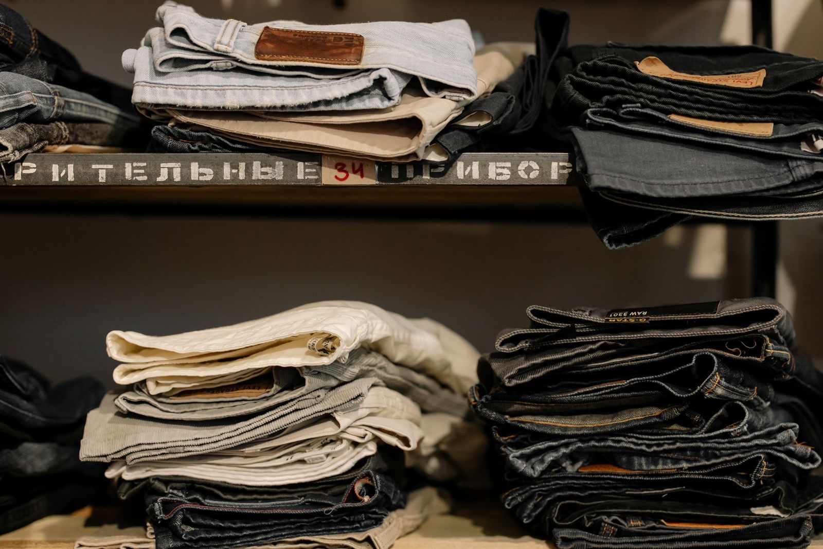 Stacks of folded jeans in light and dark washes on wooden store shelves with stenciled lettering