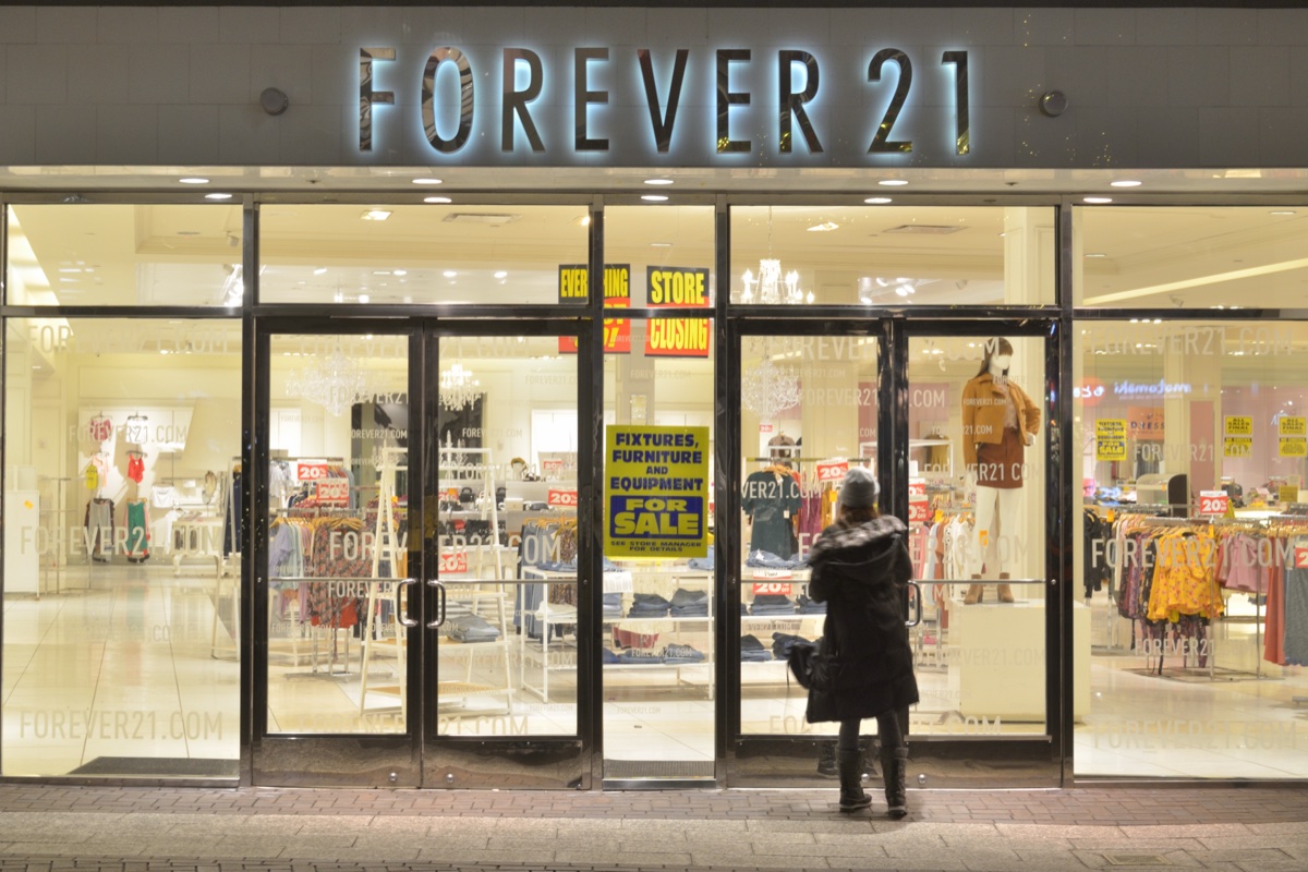 Forever 21 storefront at night with Store Closing and Everything Must Go signs in the windows and a shopper reading the fixtures-for-sale notice