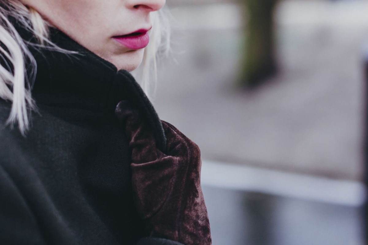 Close-up of a person's chin above the popped black collar of a wool coat, held closed with a brown velvet glove