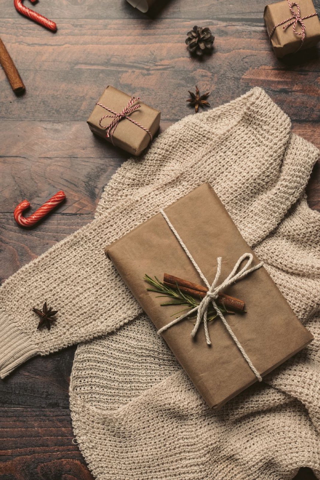 Flat lay of a kraft paper wrapped parcel tied with string resting on a cream knit sweater with smaller wrapped boxes nearby