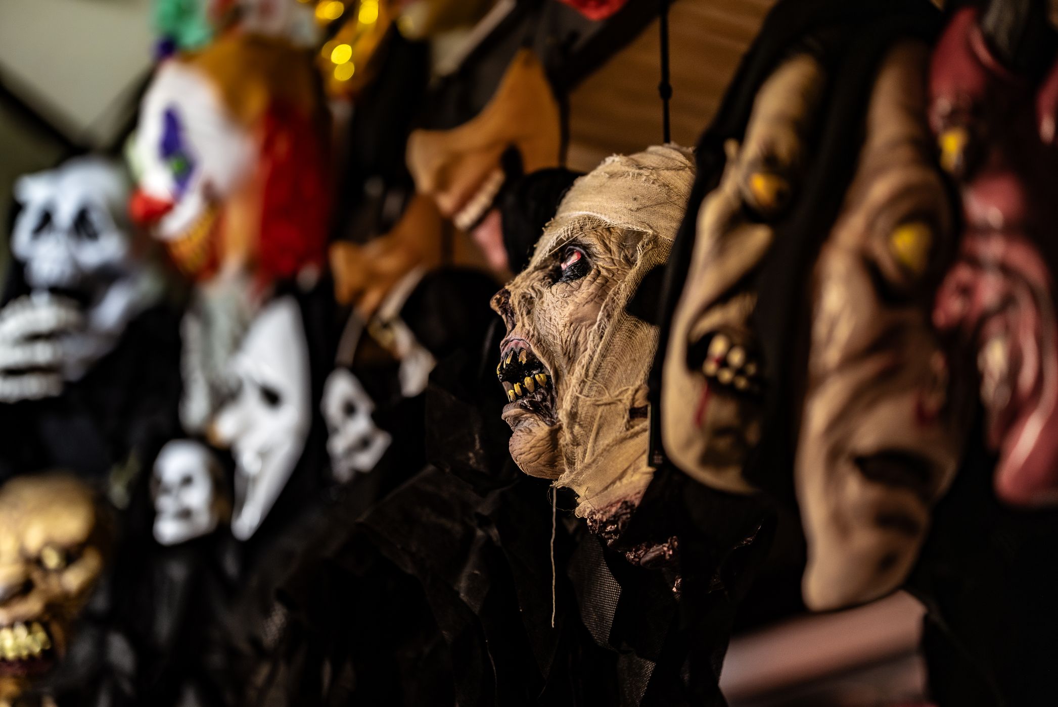 Rows of rubber horror masks including a mummy, skulls and a clown hanging on display hooks at a Halloween store