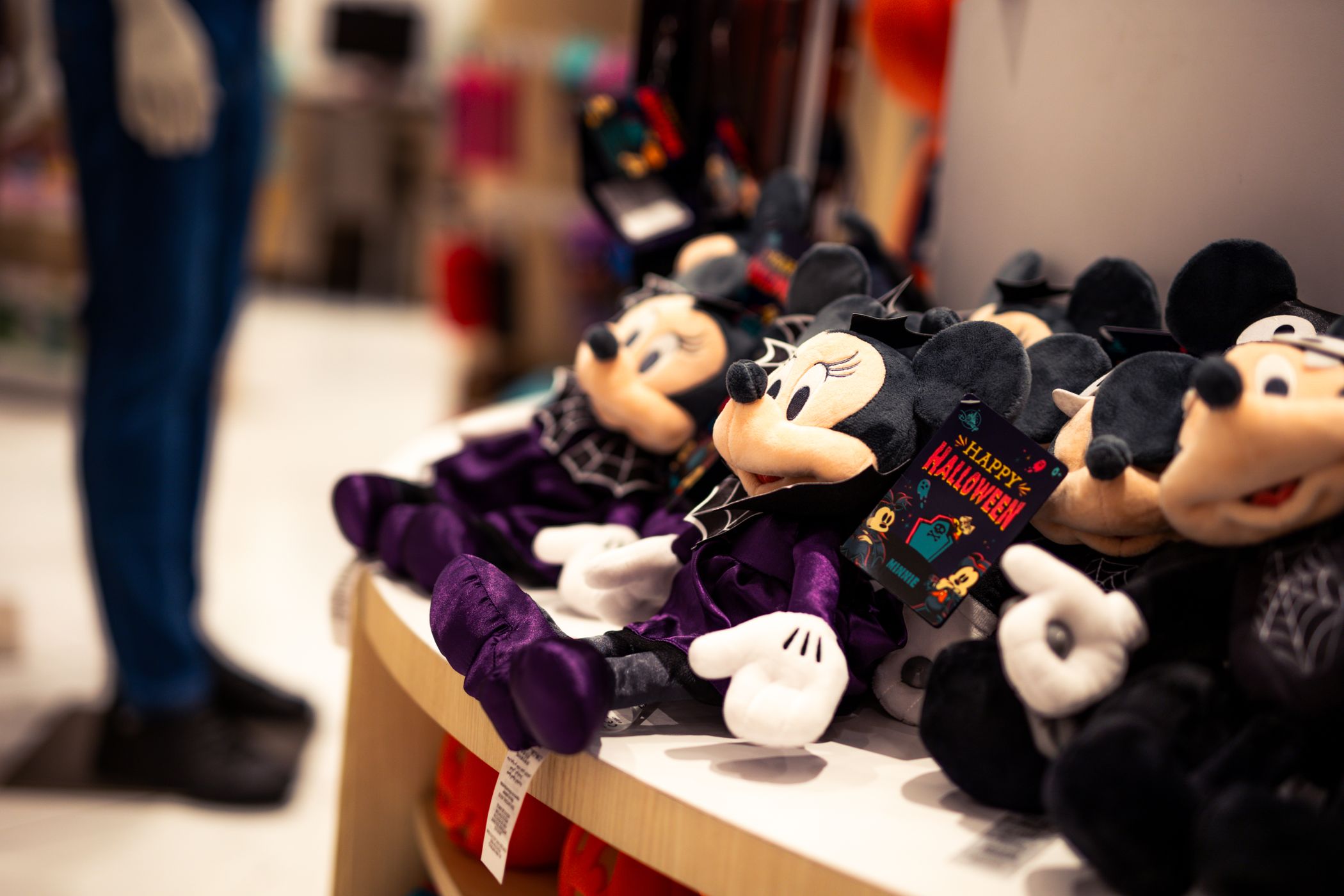 Halloween-themed Minnie Mouse plush toys in vampire capes on a store display table, one with a Happy Halloween tag attached