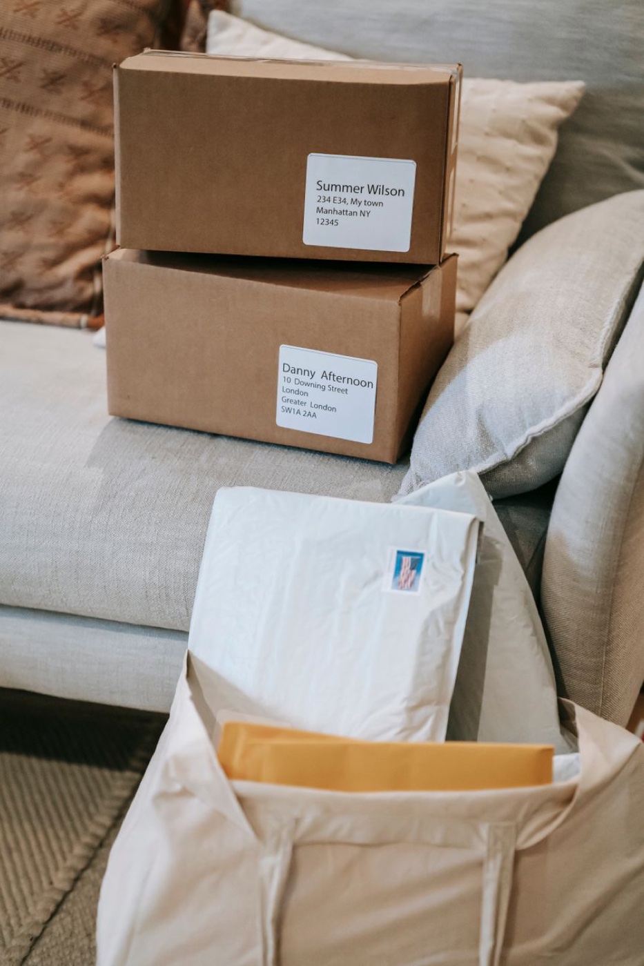 Two labelled cardboard boxes stacked on a sofa, the top one addressed to Manhattan New York and the one beneath it addressed to London