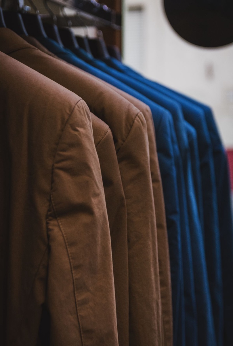 Rack of brown and blue cotton twill jackets on dark hangers in a shop, shoulders overlapping in a row